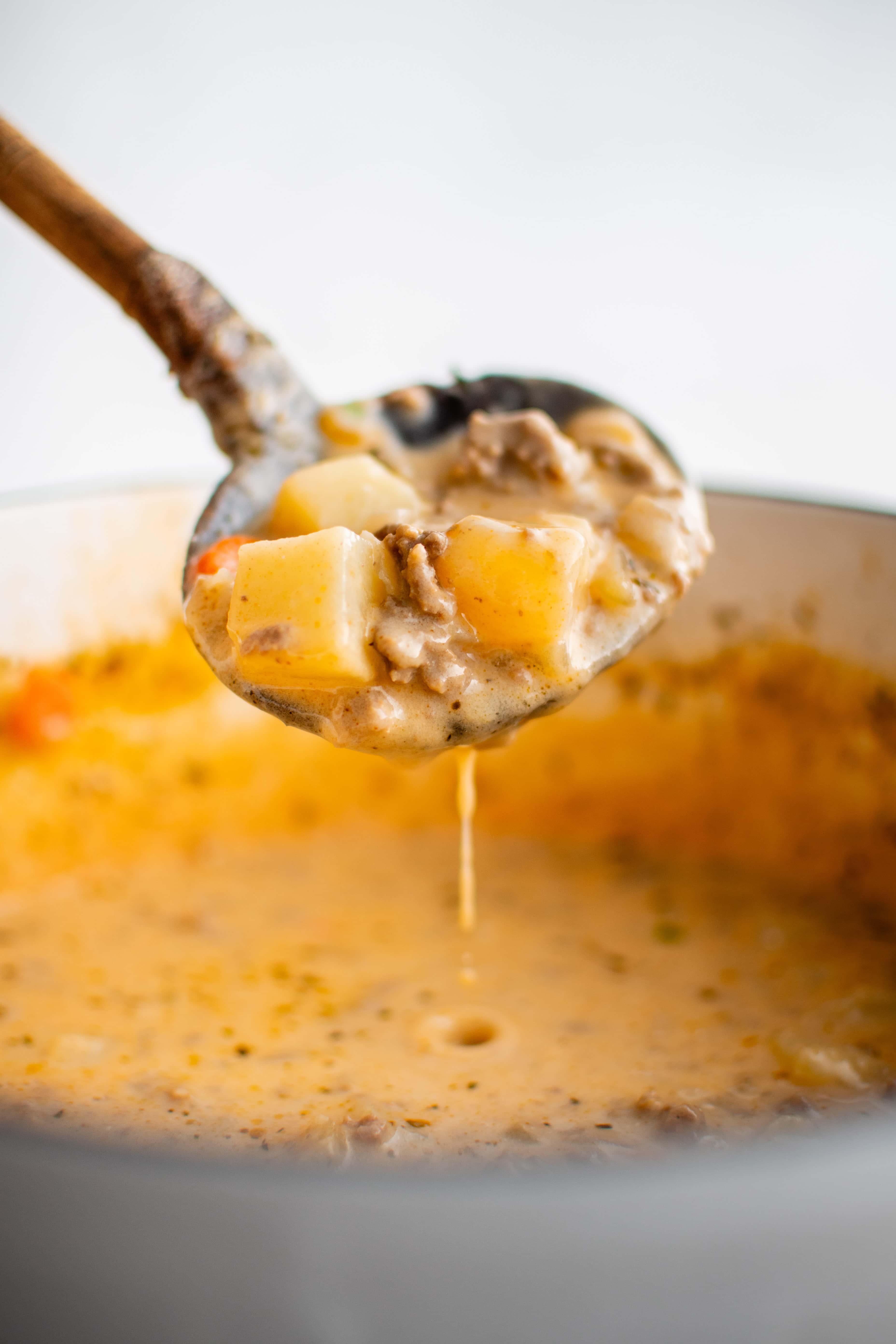 Ladle filled with cheesy cheeseburger soup with diced potatoes and ground beef in a creamy broth.