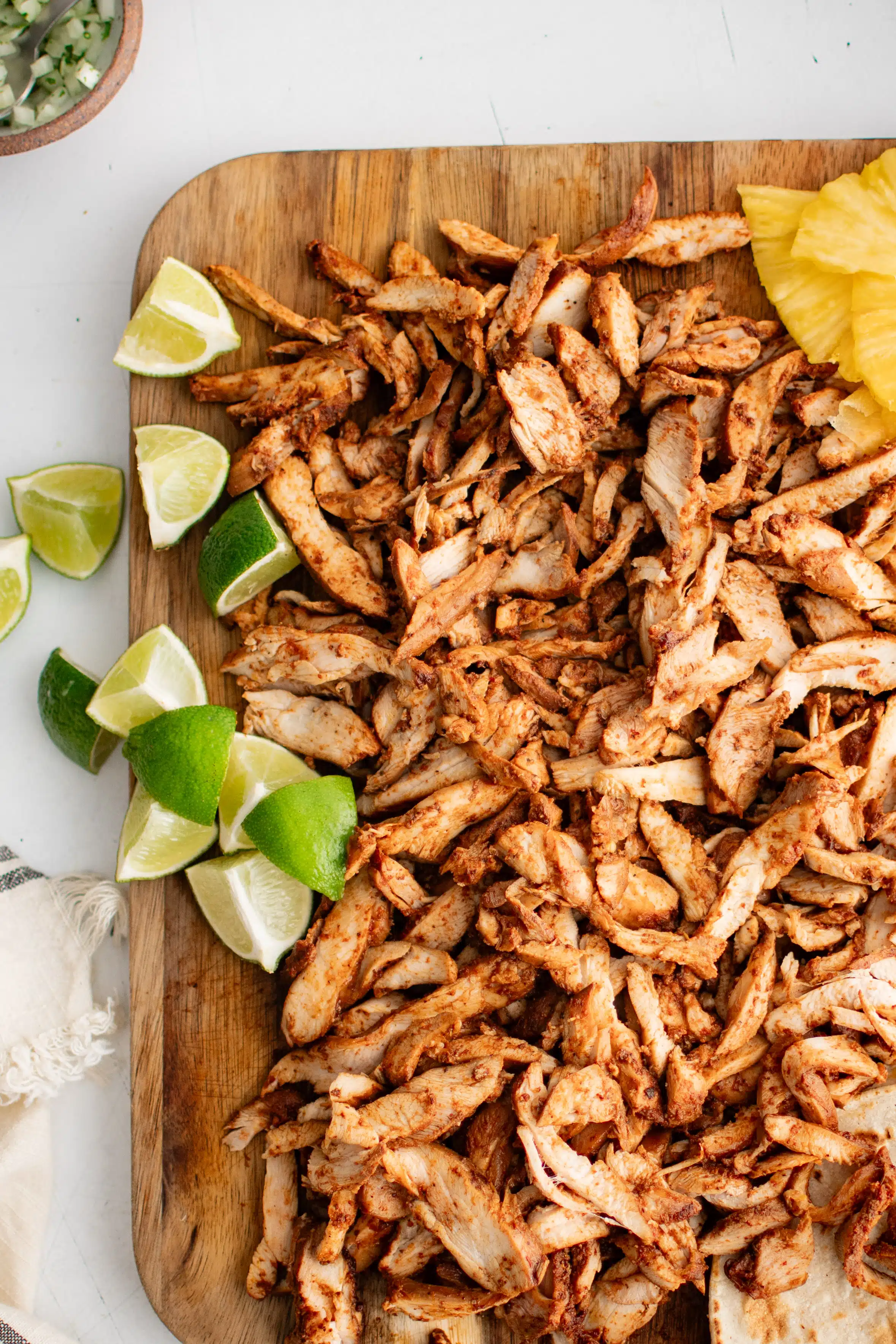 Thinly sliced chicken al pastor arranged over a large cutting board and served with sliced pineapple, flour tortillas, and lime wedges.