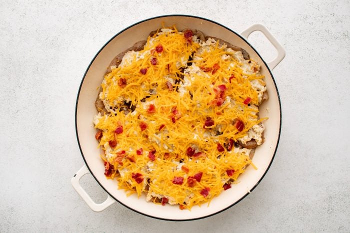 Large white oven-safe pan filled with raw, uncooked chicken breasts covered in a mixture of cream of chicken soup, cream cheese, ranch seasoning mix, shredded cheddar cheese, and cooked bacon bits.