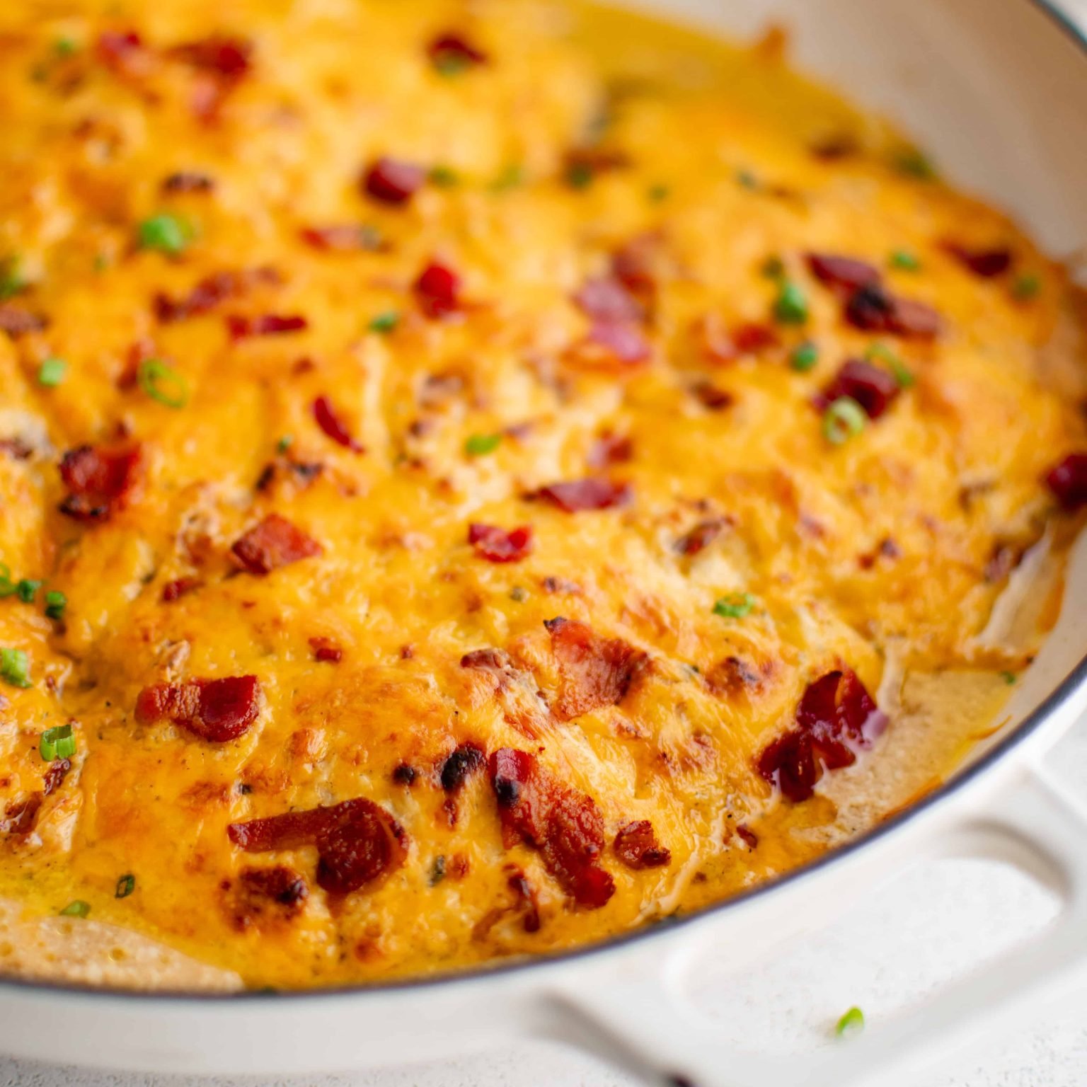 Large white oven-safe pan filled with chicken breasts covered in a mixture of cream of chicken soup, ranch seasoning mix, cream cheese, gooey melted cheddar cheese, and bacon bits.