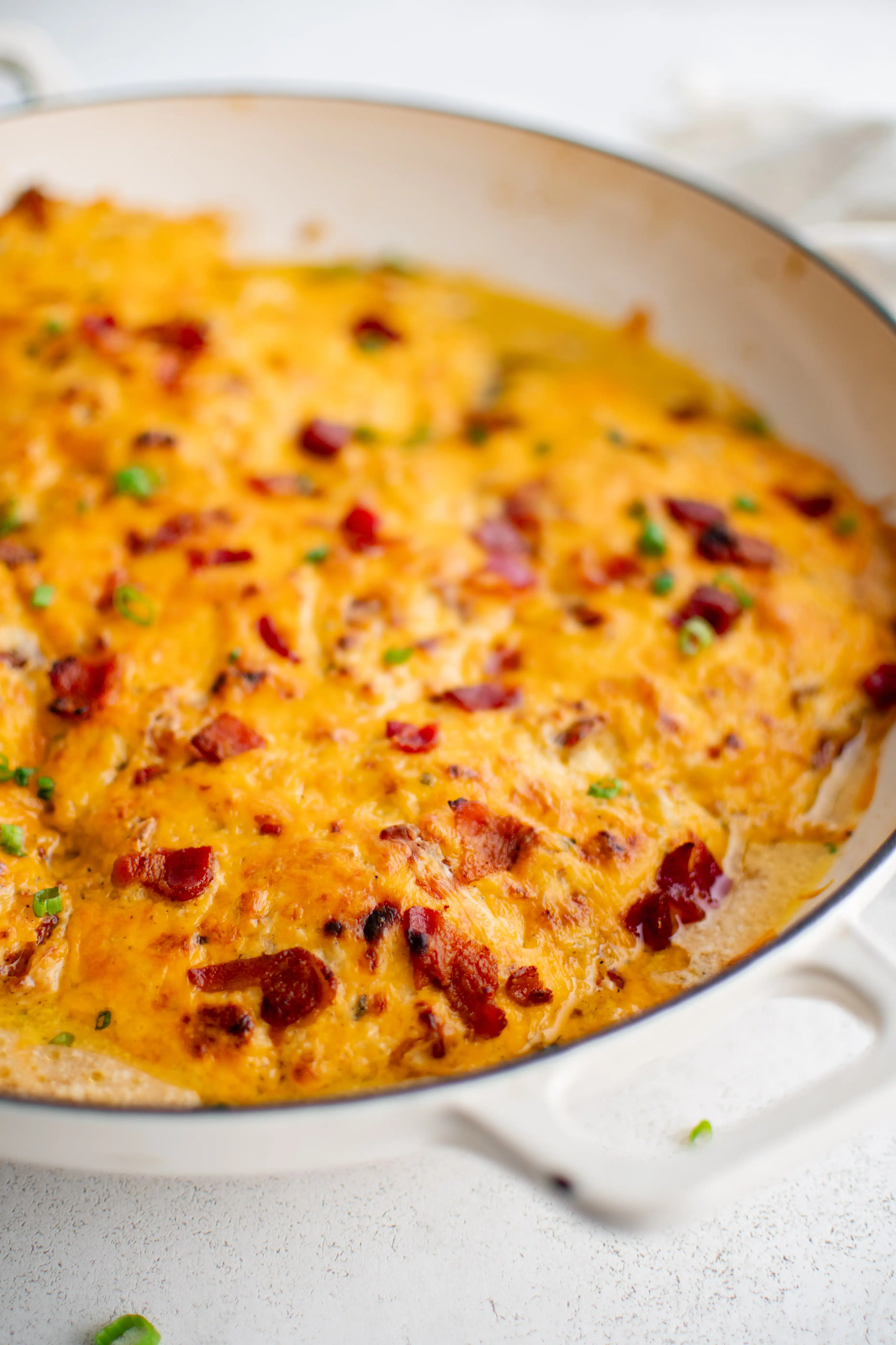 Large white oven-safe pan filled with chicken breasts covered in a mixture of cream of chicken soup, ranch seasoning mix, cream cheese, gooey melted cheddar cheese, and bacon bits.