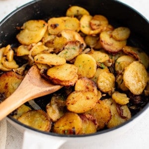 Large cast iron pan filled with crispy cooked slices of Idaho potatoes and onion seasoned with garlic powder, salt, and black pepper and garnished with fresh parsley.