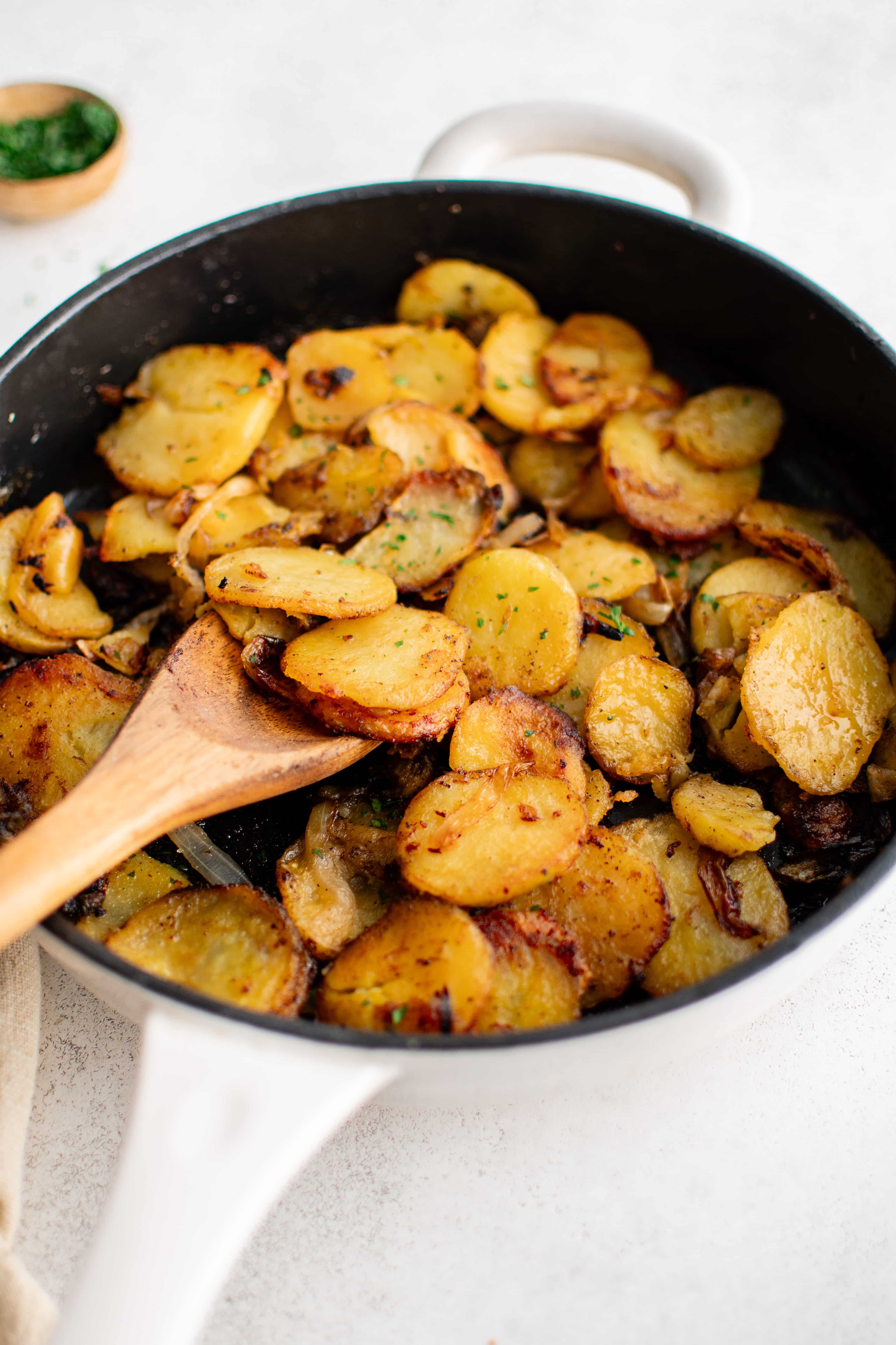 Large cast iron pan filled with crispy cooked slices of Idaho potatoes and onion seasoned with garlic powder, salt, and black pepper and garnished with fresh parsley.