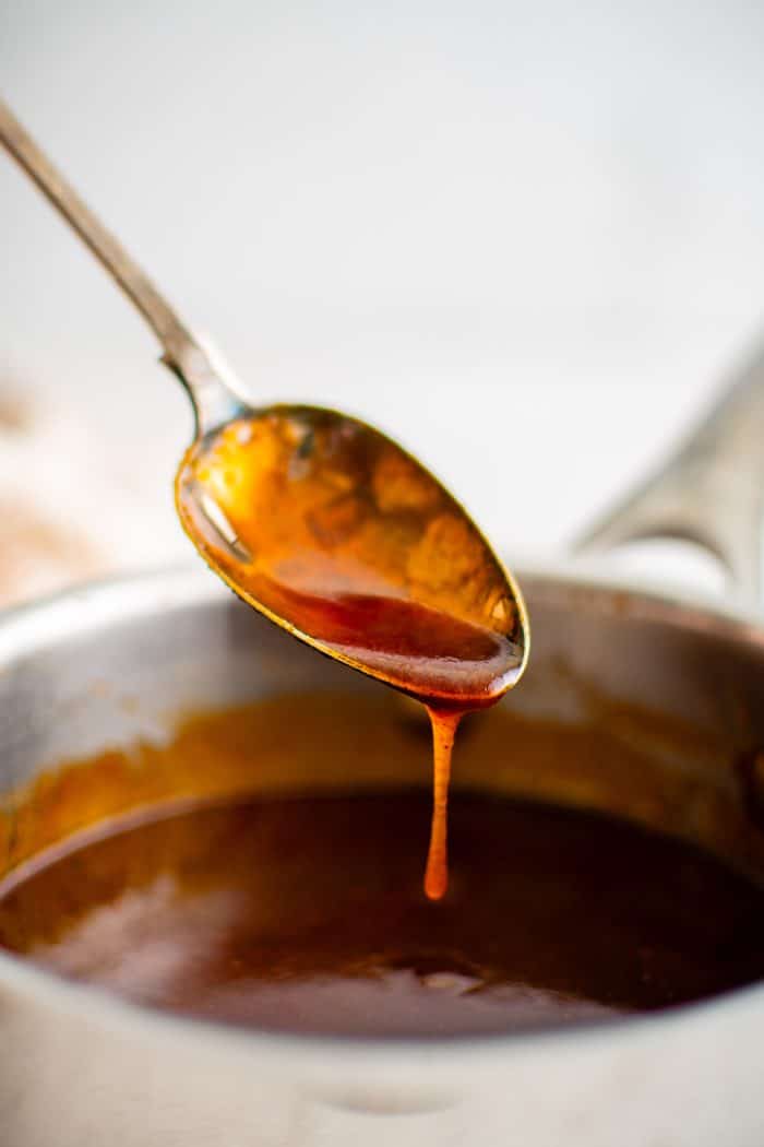 Nashville hot sauce dripping off a small teaspoon into a small sauce pot filled with homemade Nashville hot sauce.