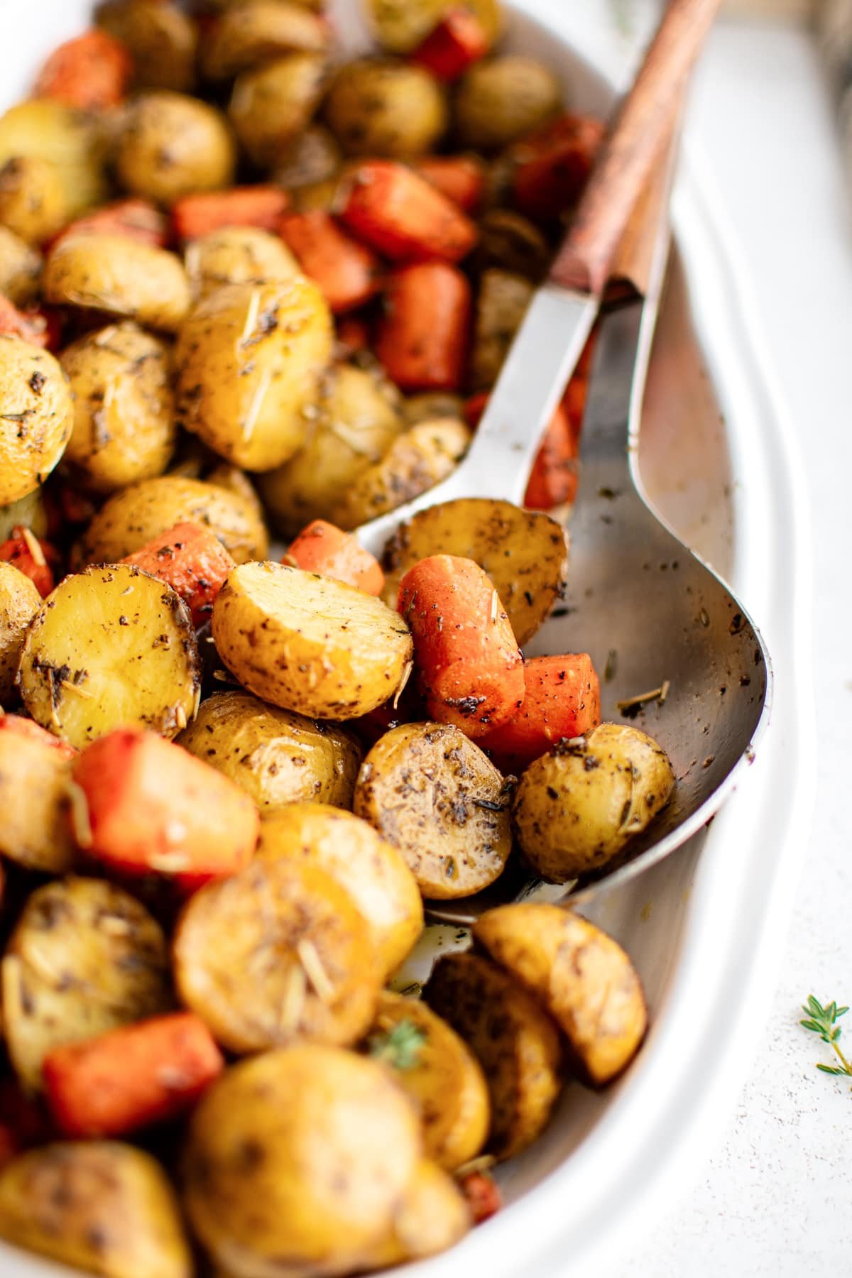 Crispy, caramelized edges of halved baby potatoes and carrots coated in herbs and seasoning served in a large white oval dish.