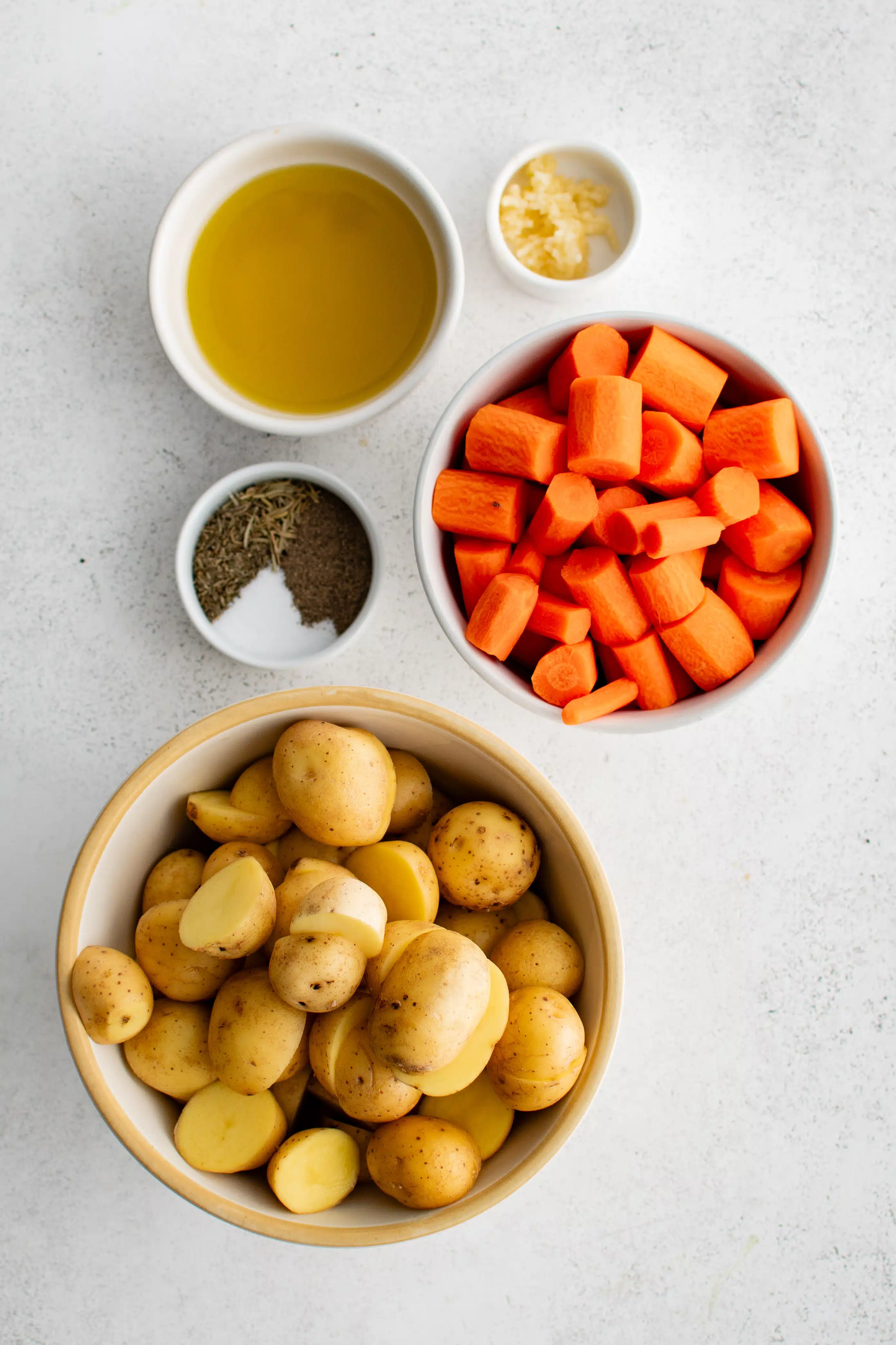 Ingredients needed to make roasted potatoes and carrots in individual measuring cups and ramekins.