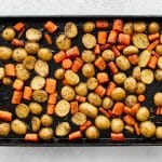 Golden roasted carrots and potatoes spread over a dark sheet pan.
