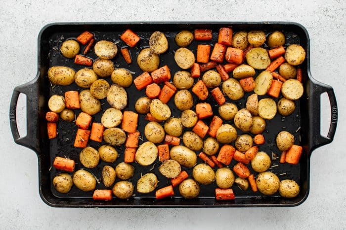Golden roasted carrots and potatoes spread over a dark sheet pan.
