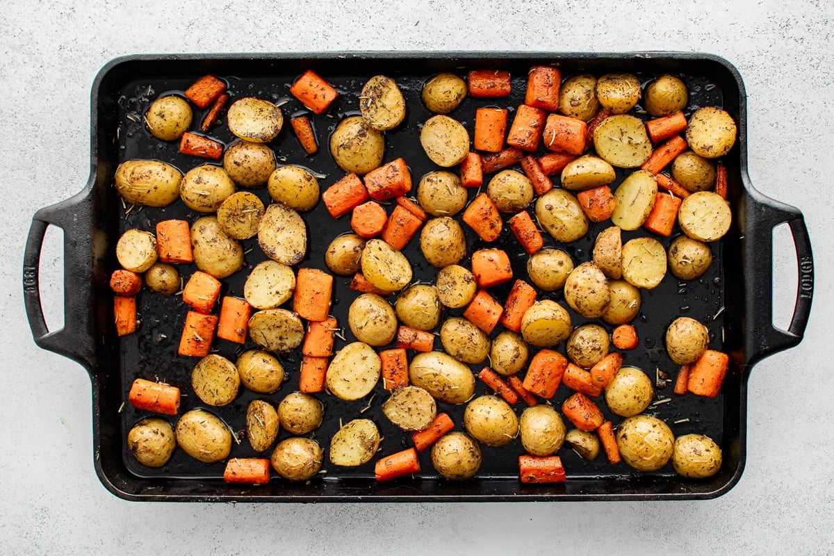 Golden roasted carrots and potatoes spread over a dark sheet pan.
