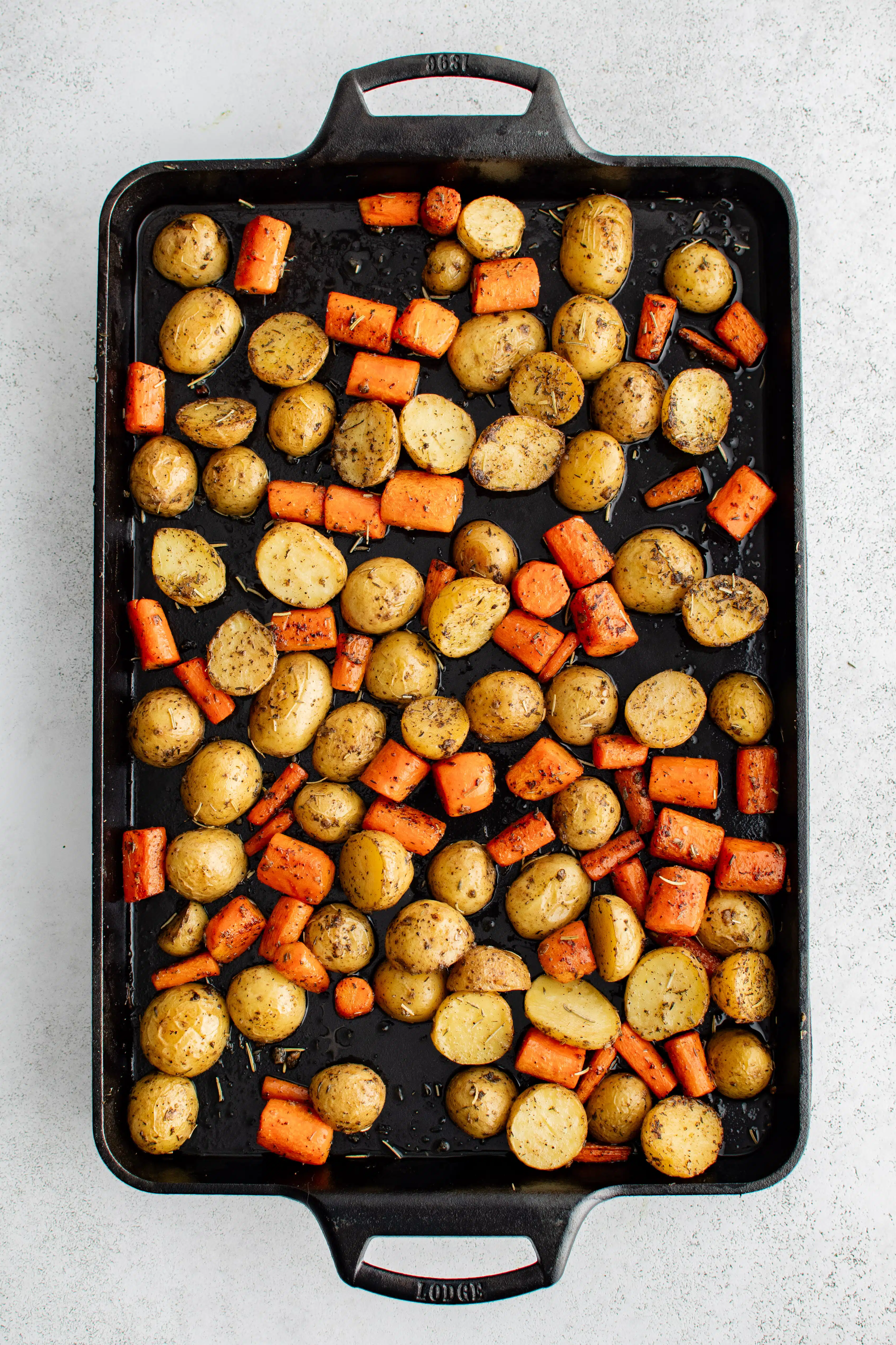 Large Lodge cast iron baking sheet pan covered with roasted halved baby potatoes and carrots.