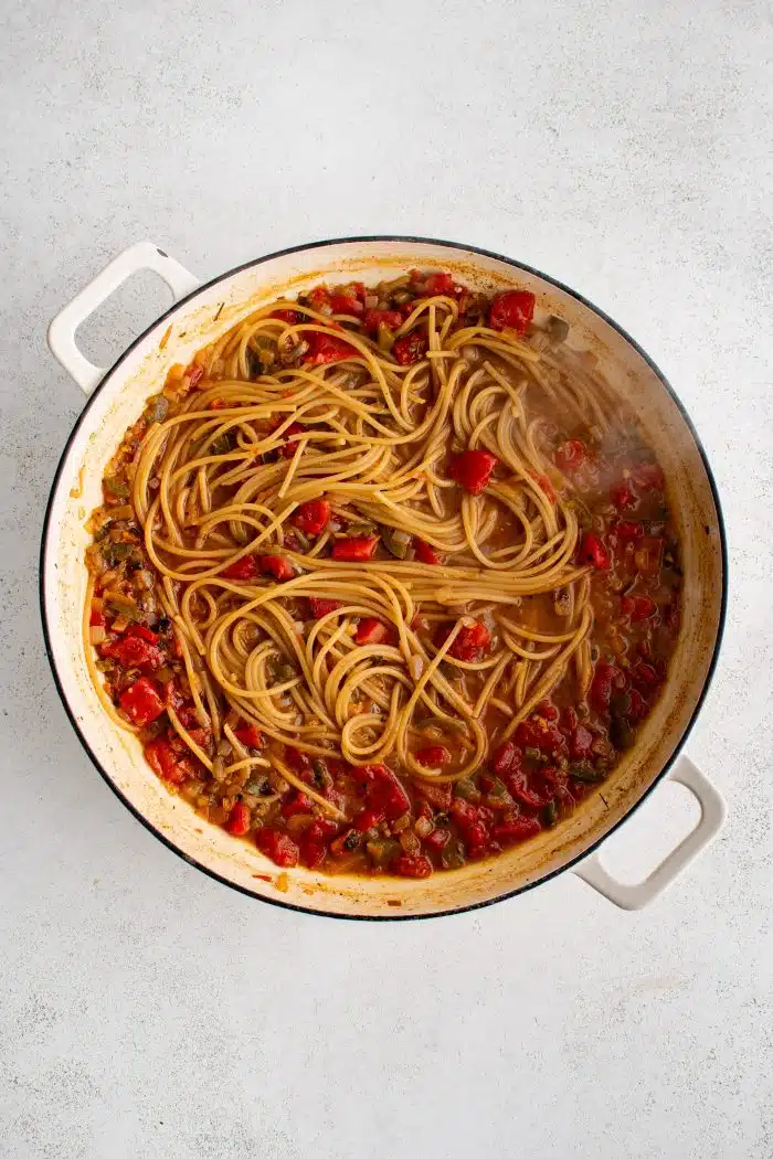 Large pot filled with cooked spaghetti noodles combined with a mixture of onions, Rotel, and seasonings and spices.