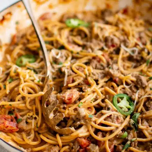 Taco spaghetti recipe filled with gooey melted cheese and seasoned ground beef in a Dutch oven garnished with jalapeno sliced and fresh minced cilantro.