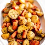 A serving platter filled with perfectly roasted baby potatoes and carrots, seasoned with herbs and spices, showcasing a golden, caramelized exterior.