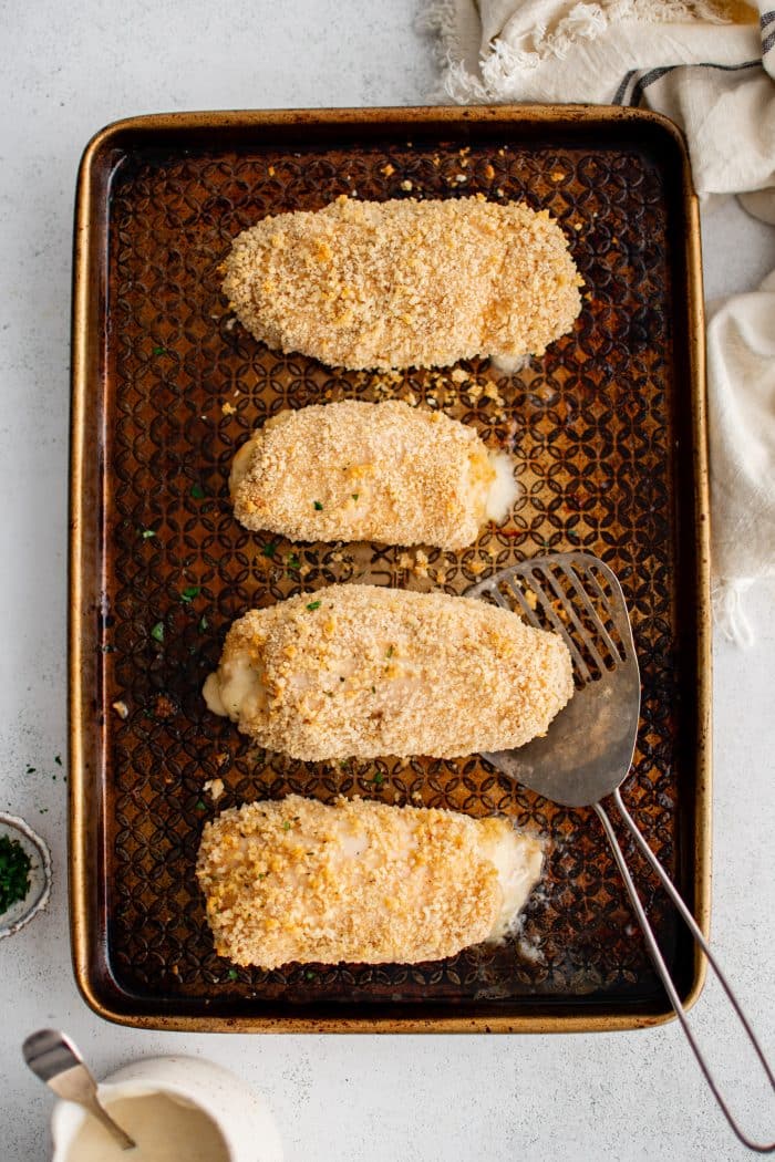 Baking sheet with four golden, crispy breadcrumb coated baked Chicken Cordon Bleu.