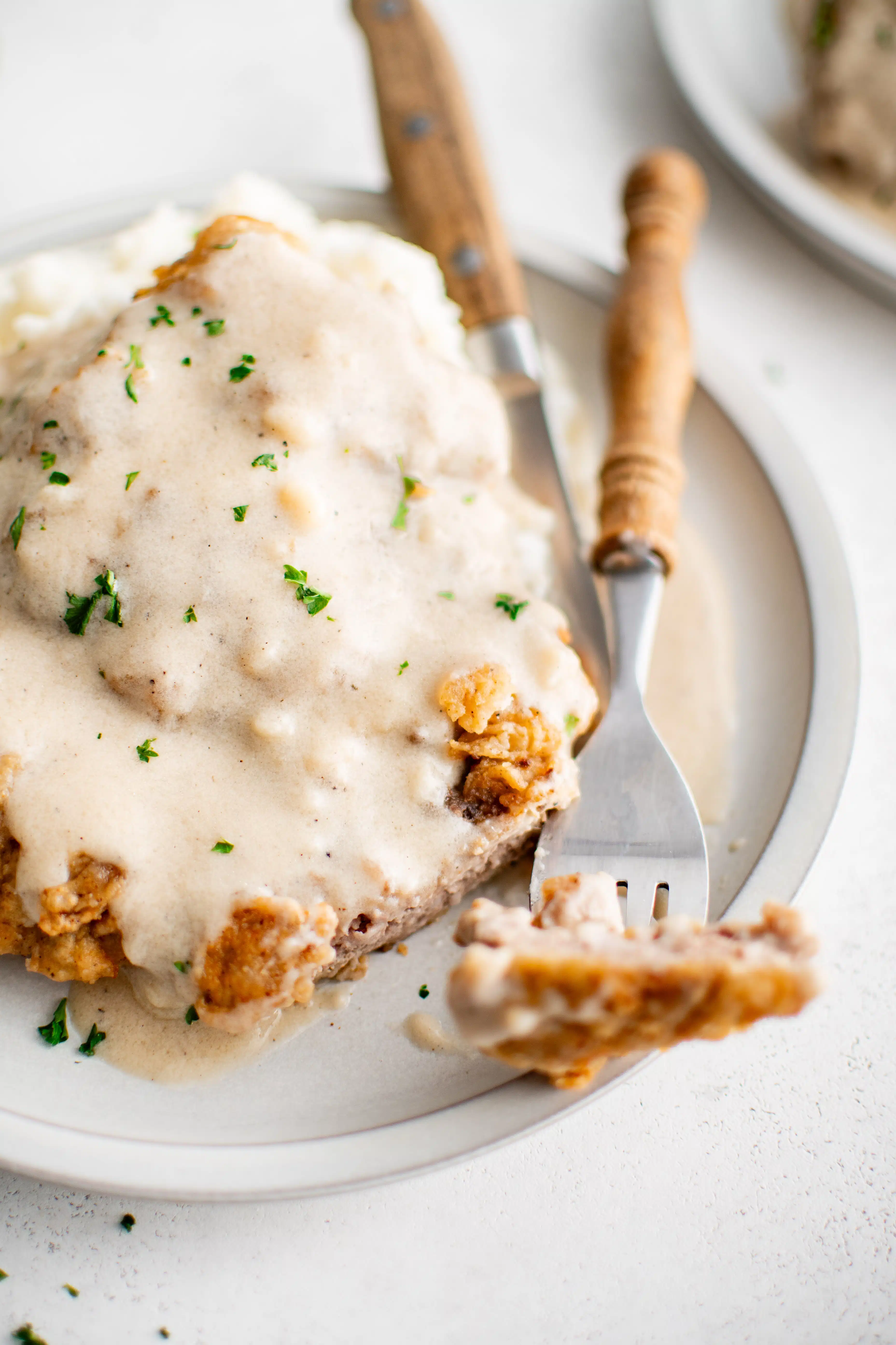 Two pieces of golden brown and crispy chicken fried steak smothered in creamy white gravy and garnished with freshly chopped parsley.