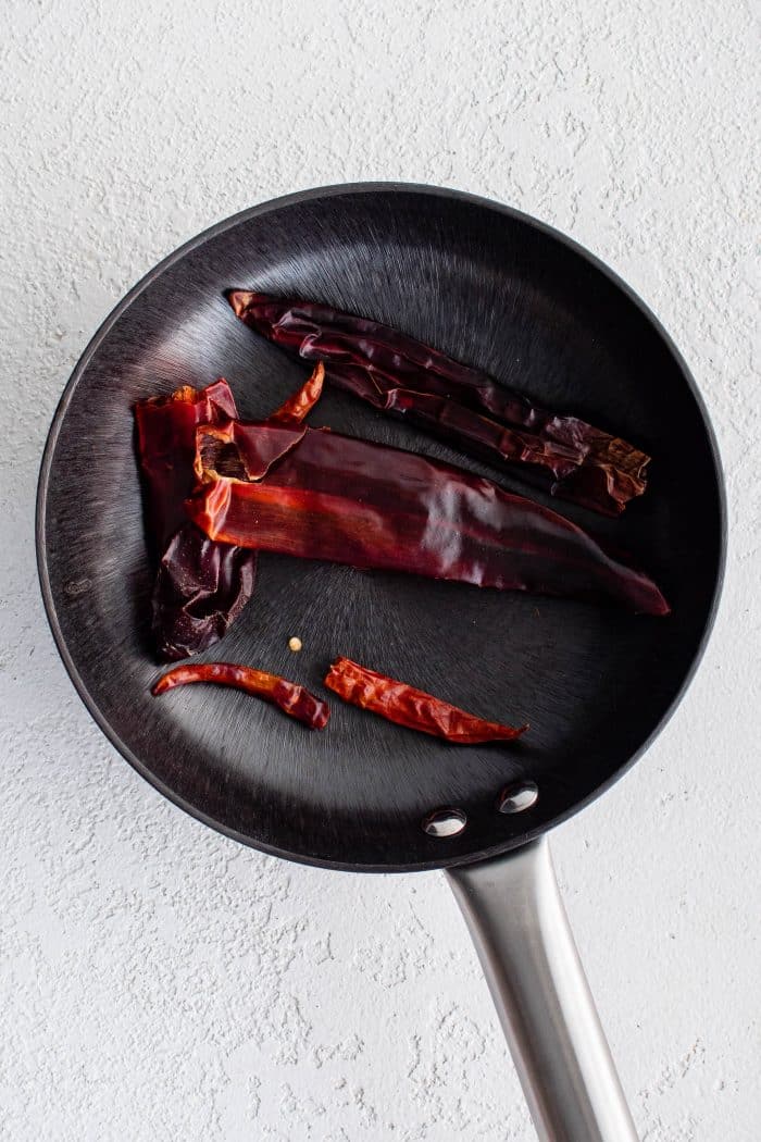 Whole dried chiles toasting in a large dry skillet.