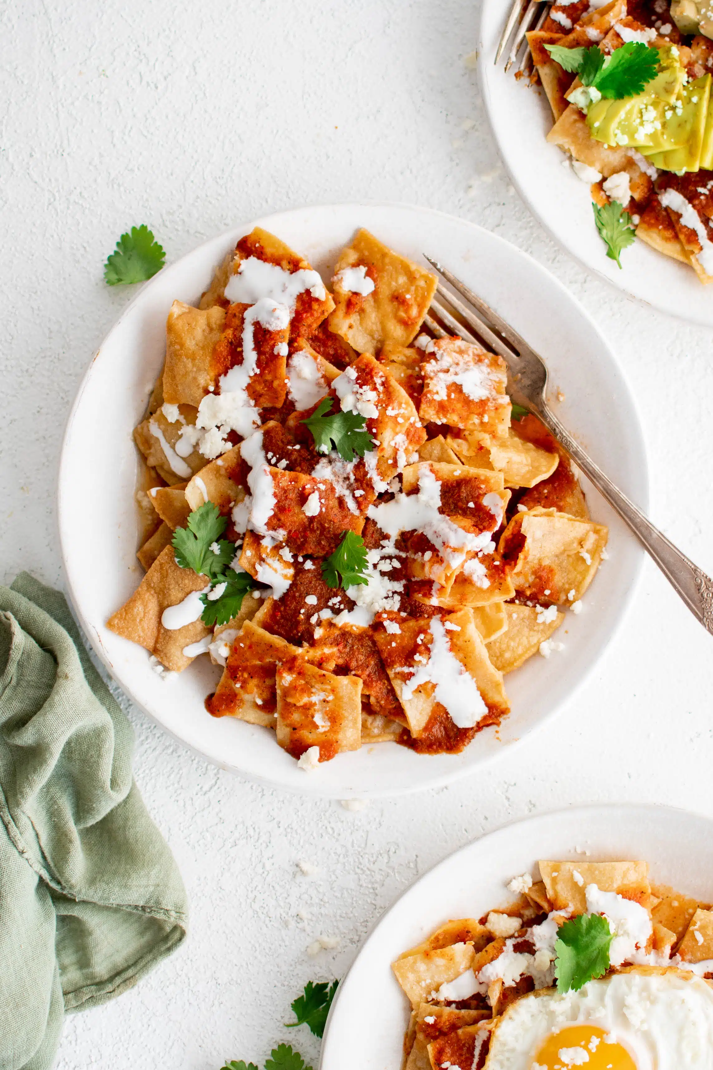 White plate filled with fried corn tortilla chips covered in salsa rojo sauce and drizzled with crema and crumbled cojita cheese and fresh cilantro.