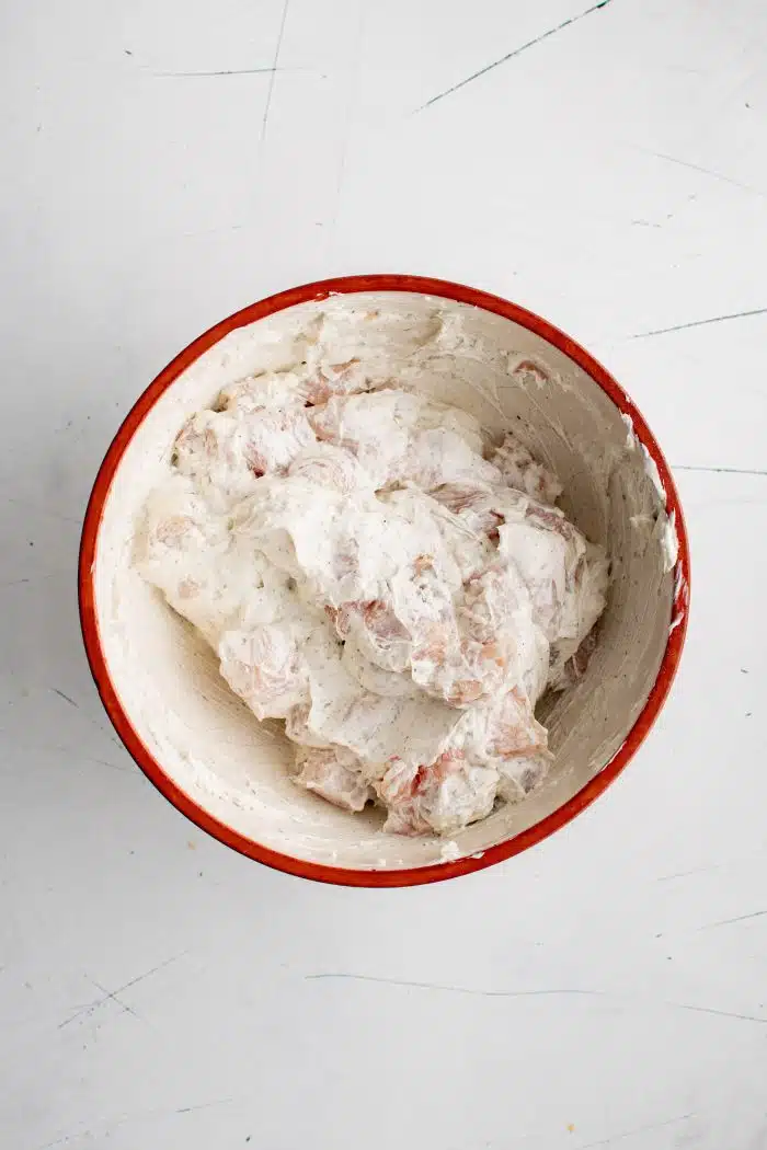 Large white mixing bowl filled with chopped chicken breast mixed with whisked together sour cream, ranch seasoning, salt, and black pepper.