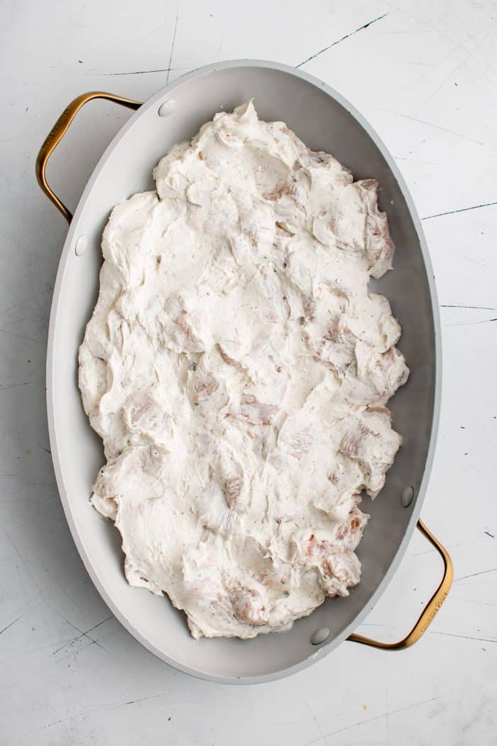 Prepared casserole dish filled with cream cheese and ranch coated chicken pieces.