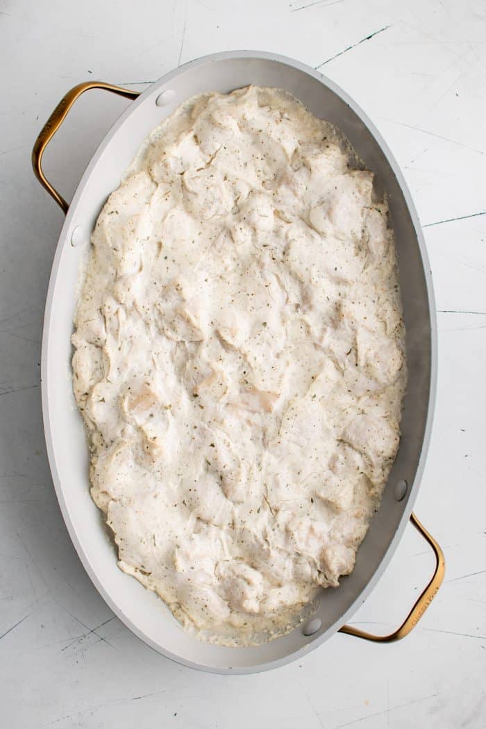 Partially baked cream cheese and ranch coated chicken pieces in a large non-stick casserole dish.