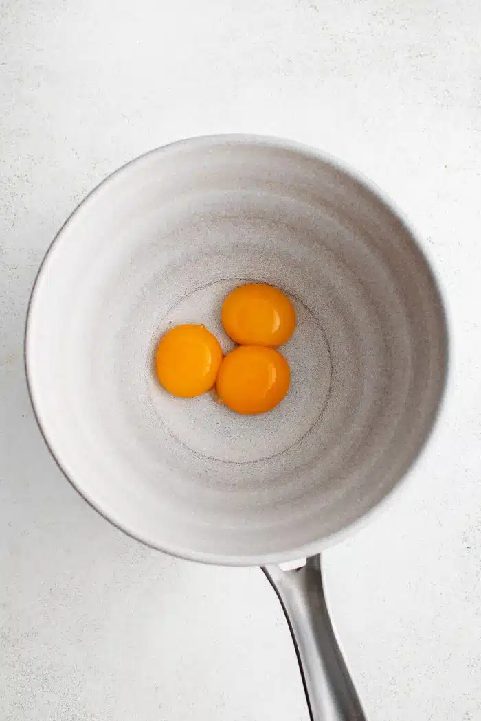 Three egg yolks in a medium saucepan.