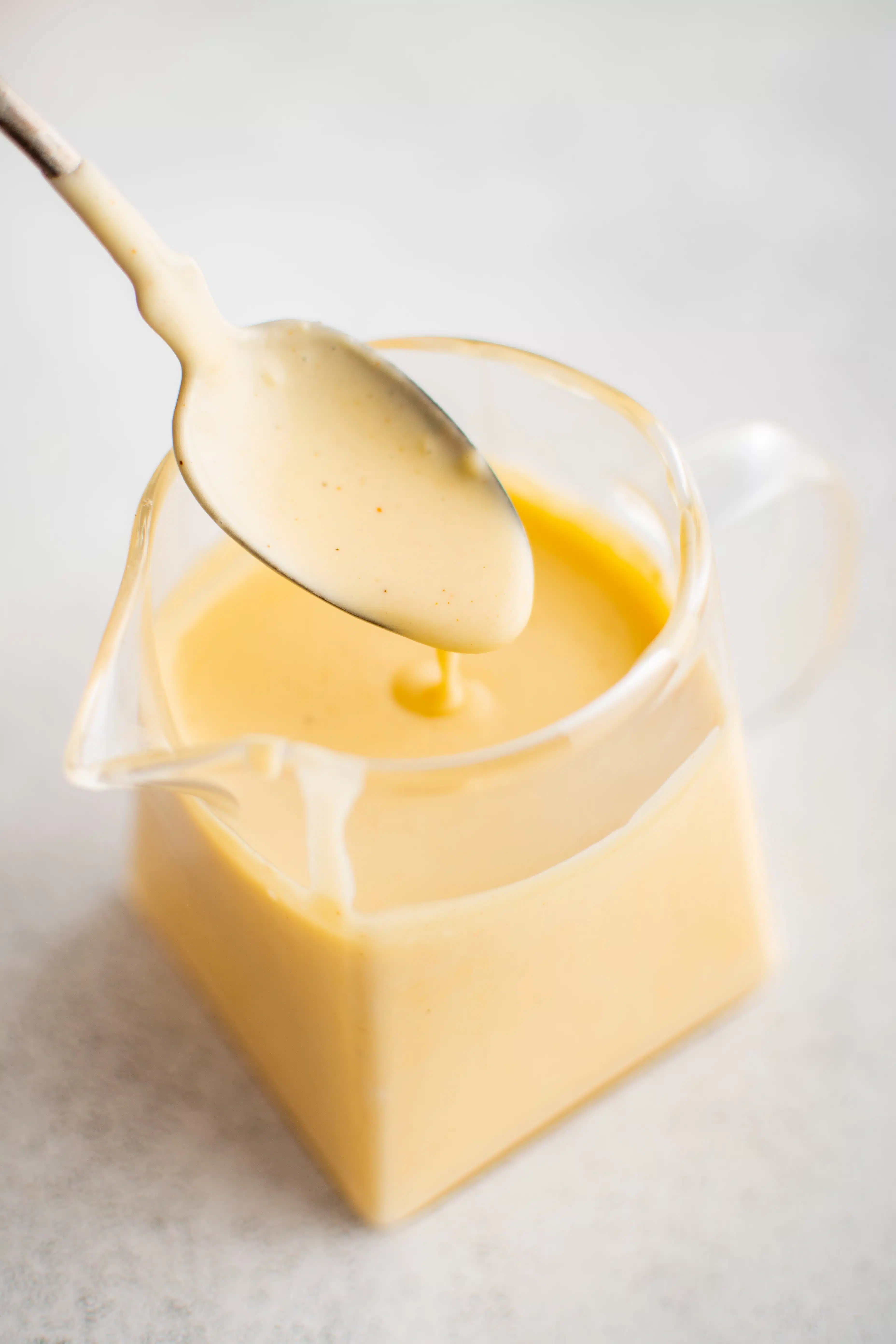 Small glass jar filled with homemade hollandaise sauce with a small spoon filled with hollandaise sauce hovering above.
