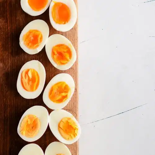 Halved hard boiled eggs on a wooden cutting board displaying the difference between the yolks from six minutes cook time to twelve minutes.