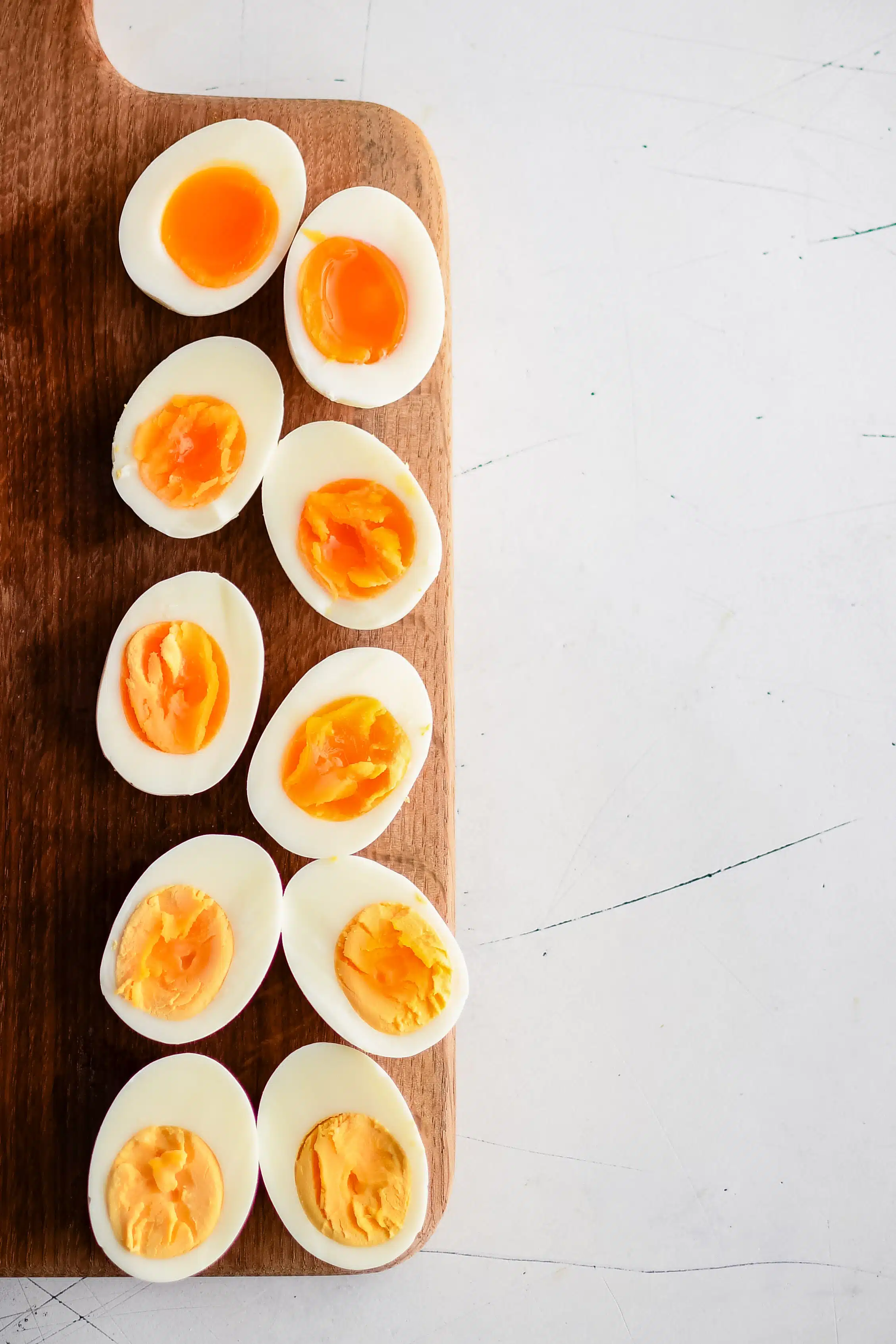 Halved hard boiled eggs on a wooden cutting board displaying the difference between the yolks from six minutes cook time to twelve minutes.