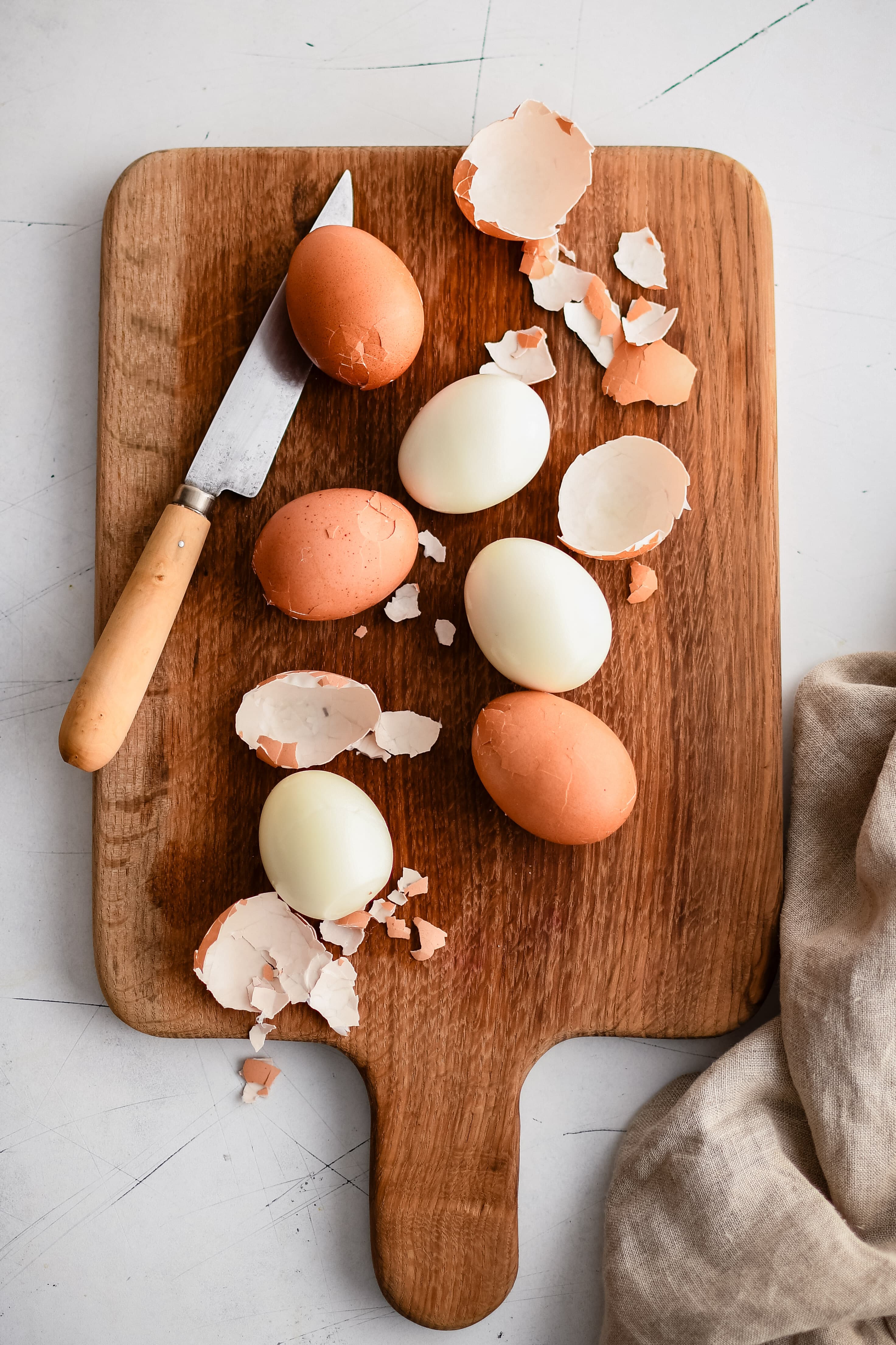 Wooden cutting board with three peeled hard-boiled eggs and three unpeeled hard-boiled eggs.
