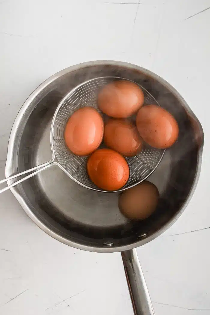 Slowly lowering fresh eggs into a pot filled with boiling water using a slotted spoon.