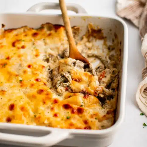 White casserole dish filled with gooey, cheesy Philly cheesesteak casserole.