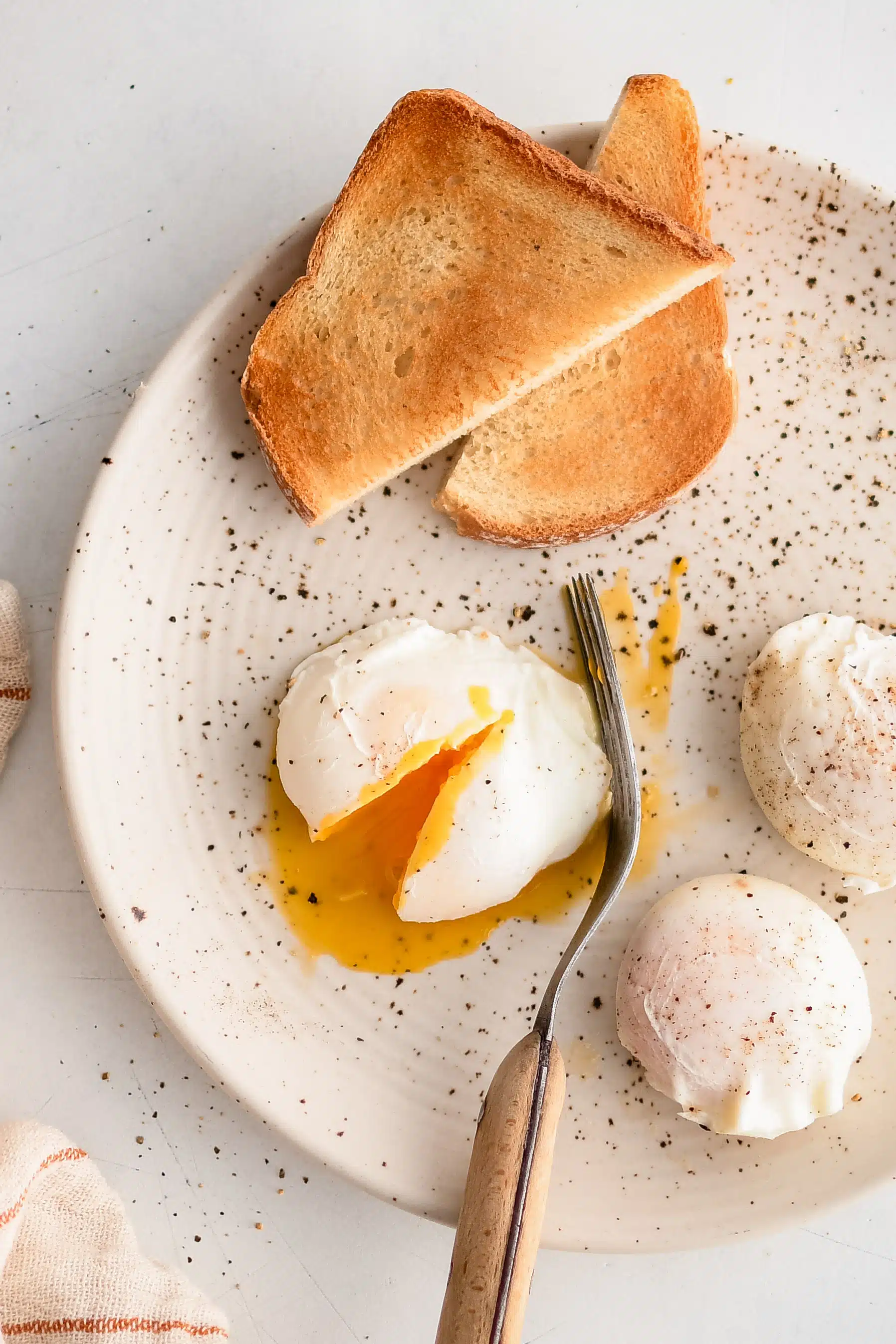 White plate with toasted white bread and three poached eggs seasoned with pepper.