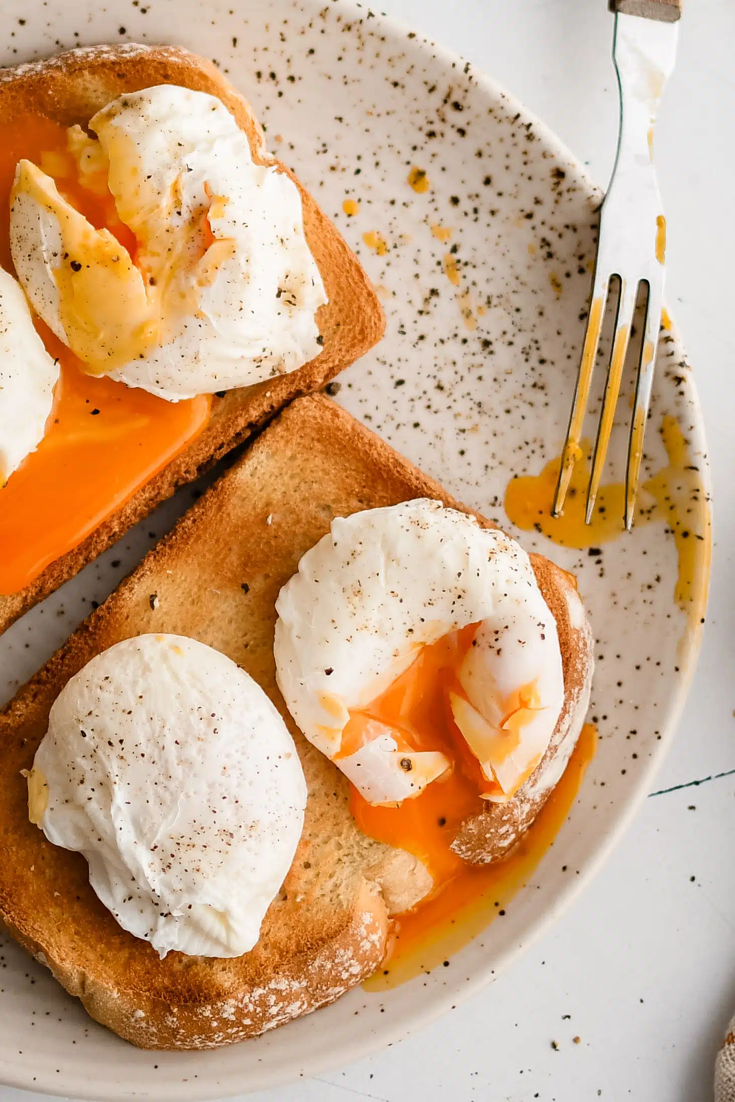 Sliced open poached eggs on toasted bread with runny yolk dripping onto the toast and seasoned with black pepper.