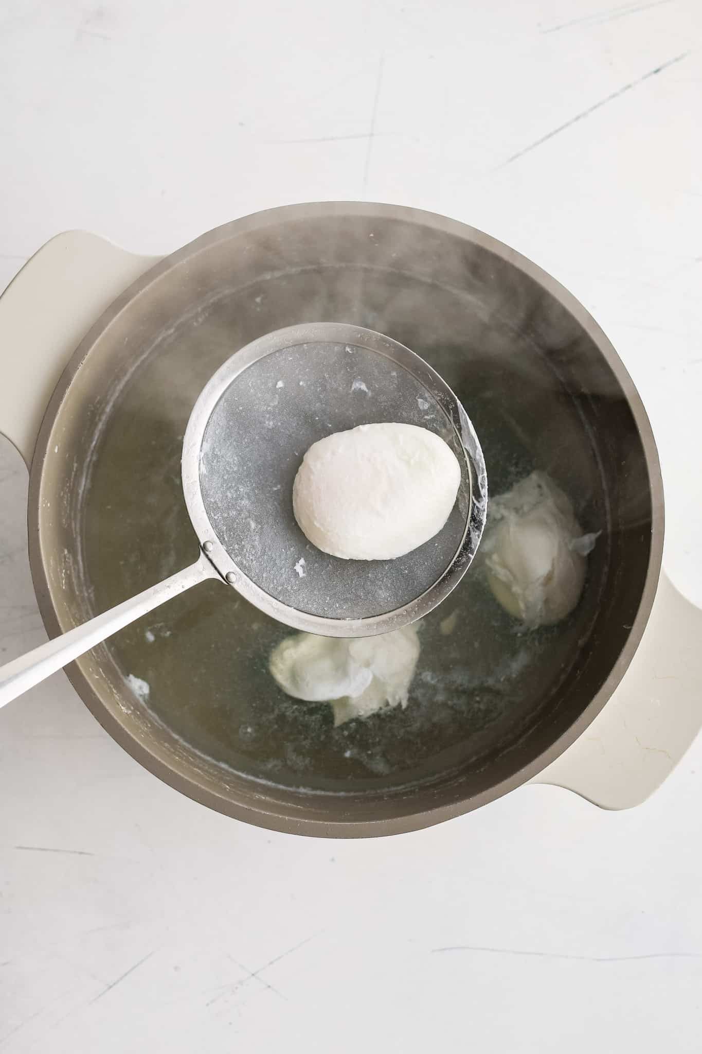 Large slotted spoon removing a perfectly poached egg from a pot filled with simmering water.