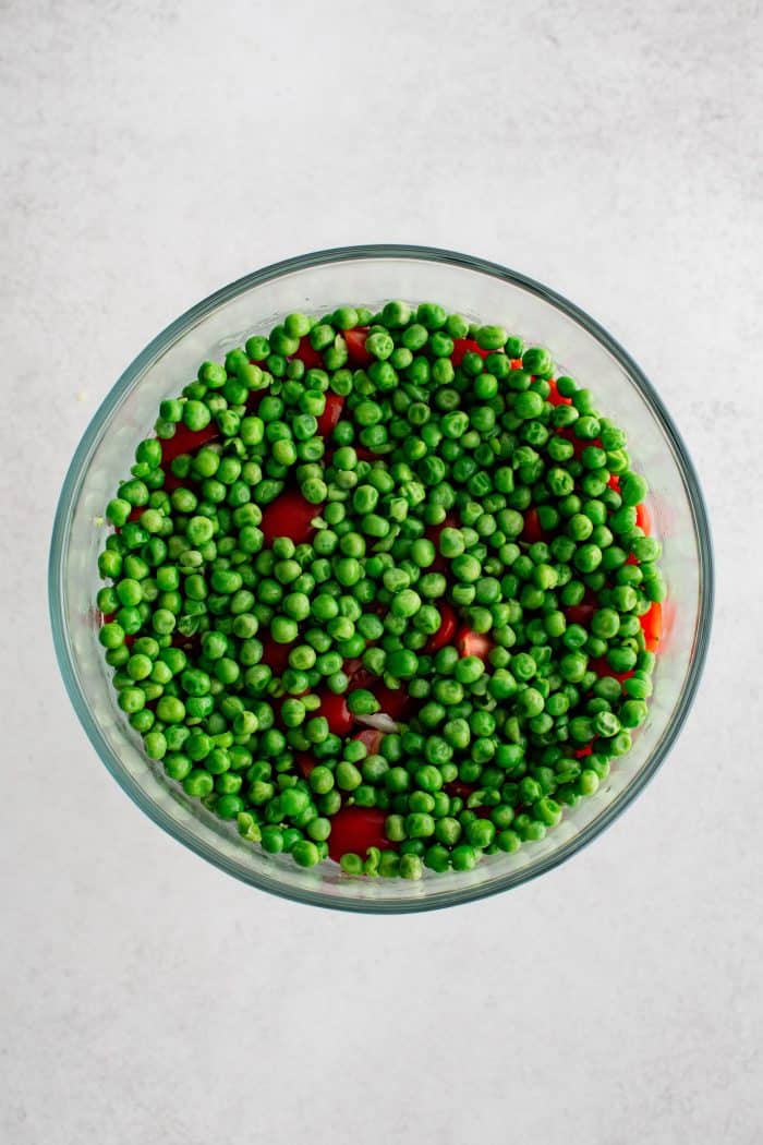 Glass bowl filled with a layer of green peas on top of sliced cherry tomatoes.