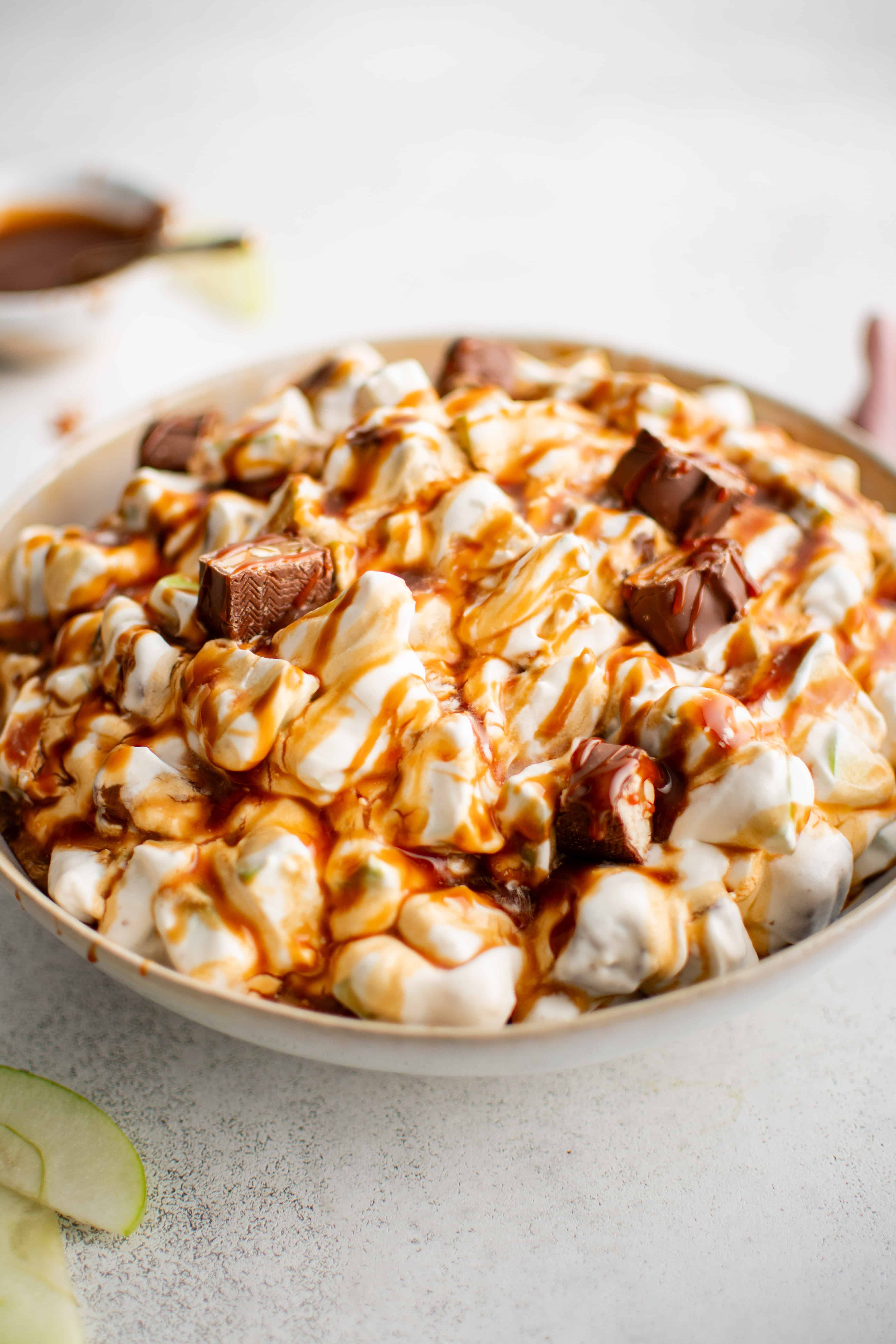 Snickers salad in a large white serving bowl drizzled with caramel sauce.