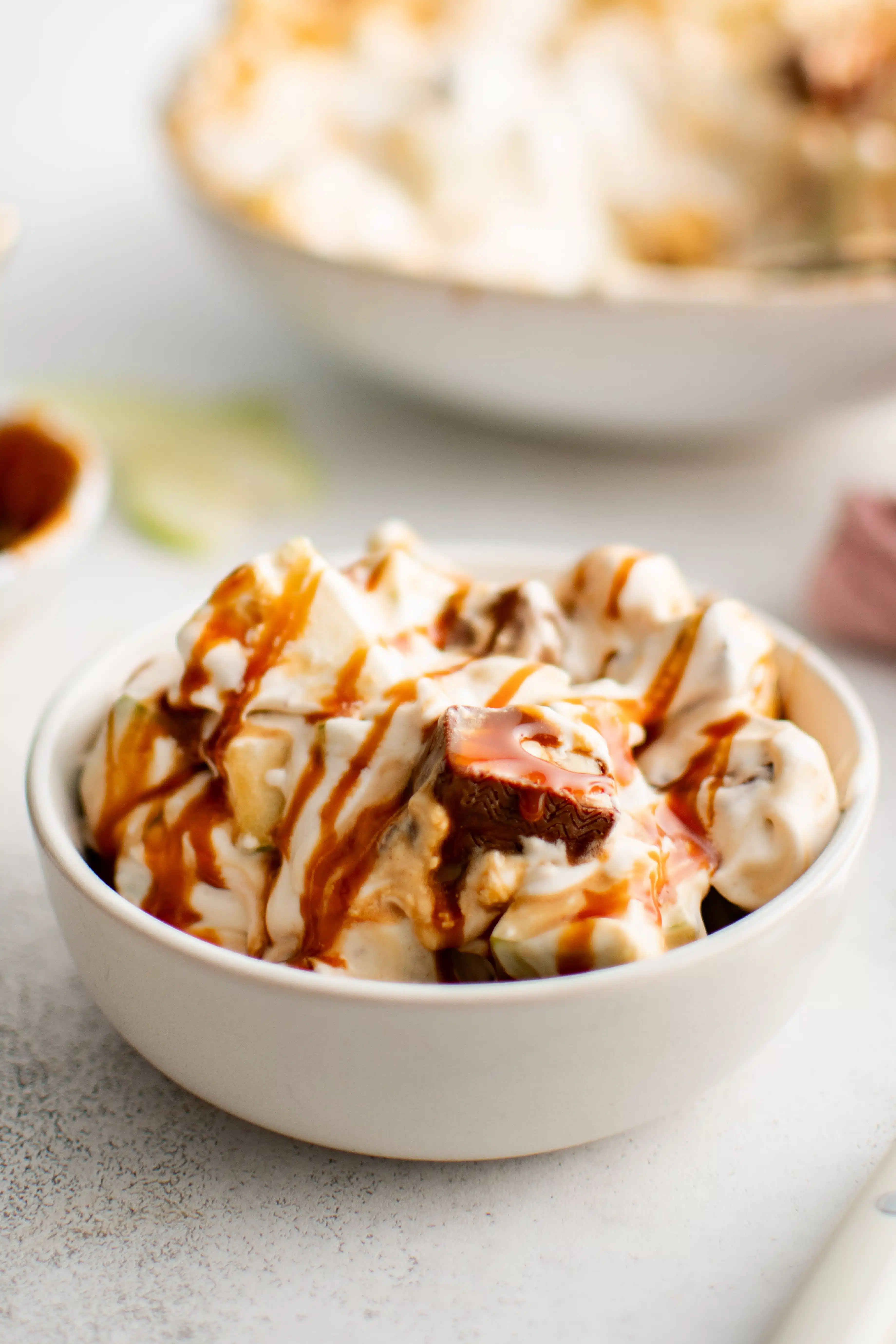 Small dessert bowl filled with Snickers salad drizzled with caramel sauce.
