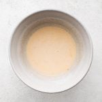 Mixing bowl filled with whisked together buttermilk, eggm and hot sauce.