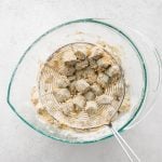 Shaking excess flour, cornmeal, garlic powder, onion powder, salt, pepper, and paprika mixture from 1-inch pieces of chopped okra coated in all-purpose flour.