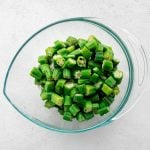 Large glass mixing bowl filled with 1-inch pieces of chopped okra.