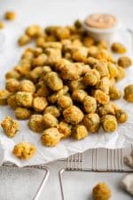Perfectly golden and crispy deep-fried okra on a large piece of parchment paper set over a wire rack and served with a creamy mayo sauce for dipping.
