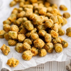 Perfectly golden and crispy deep-fried okra on a large piece of parchment paper set over a wire rack and served with a creamy mayo sauce for dipping.