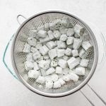 Shaking excess flour from 1-inch pieces of chopped okra coated in all-purpose flour.