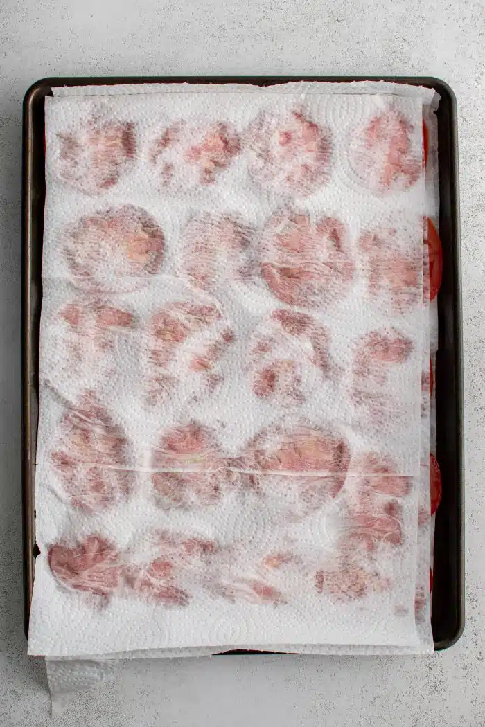 Large baking sheet with sliced tomatoes between sheets of paper towels.