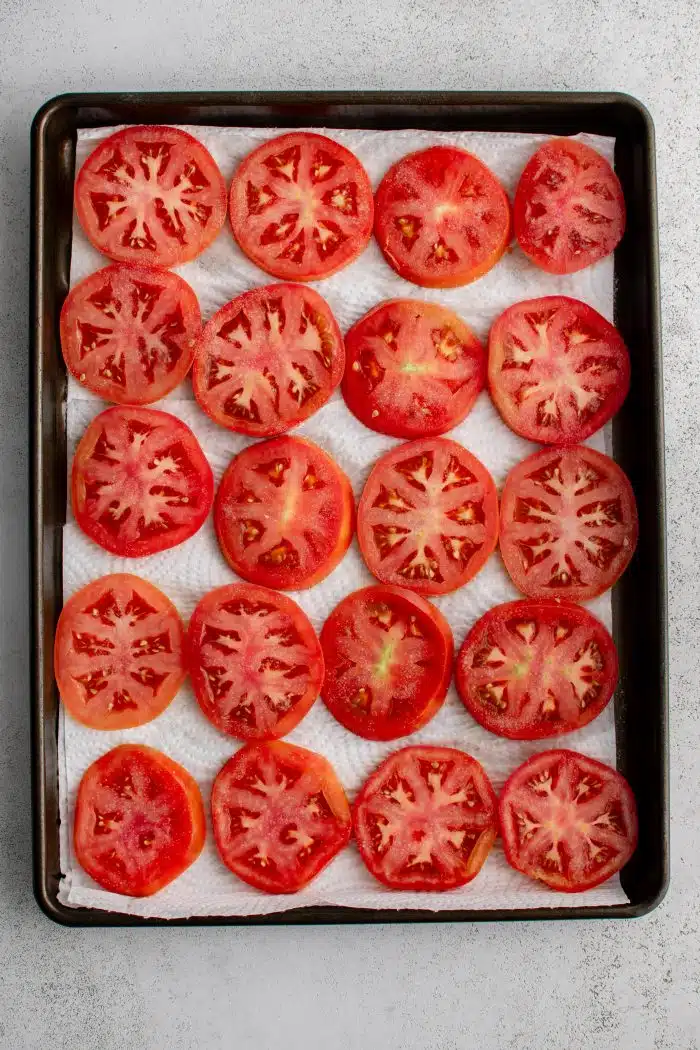 Large baking sheet with sliced tomatoes on top of paper towels.