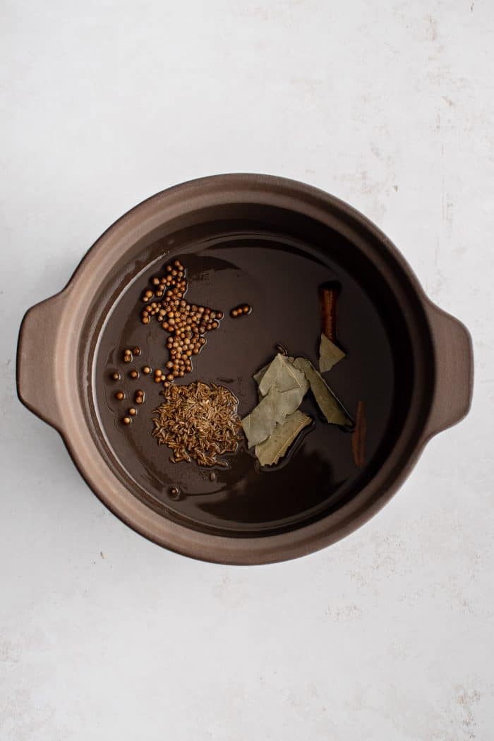 Toasting bay leaves, cumin seeds, coriander seeds, and cinnamon with oil in a large pot.