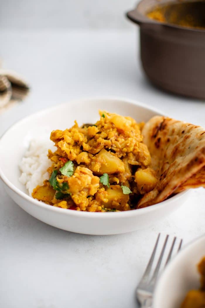 White shallow bowl filled with white rice and aloo gobi with a side of homemade paratha.