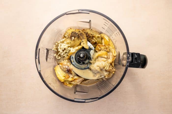 Roasted eggplant, tahini, garlic, lemon juice, salt, and pepper added to a food processor bowl.