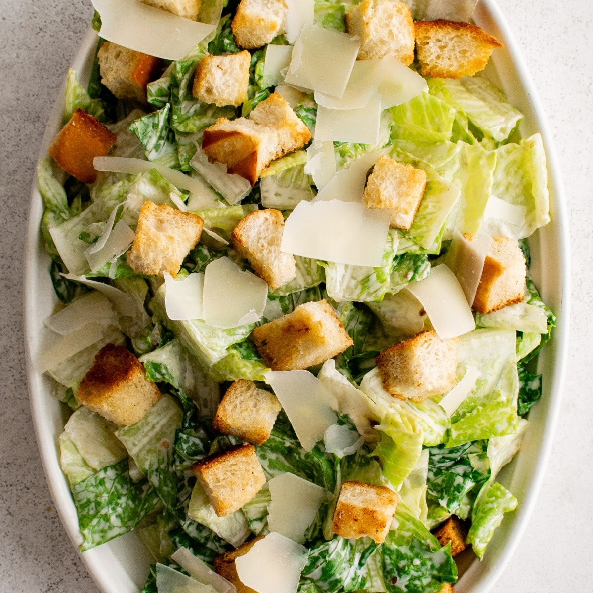 Oval salad plate filled with romaine lettuce tossed in homemade Caesar salad dressing, homemade croutons and shaved parmesan cheese.