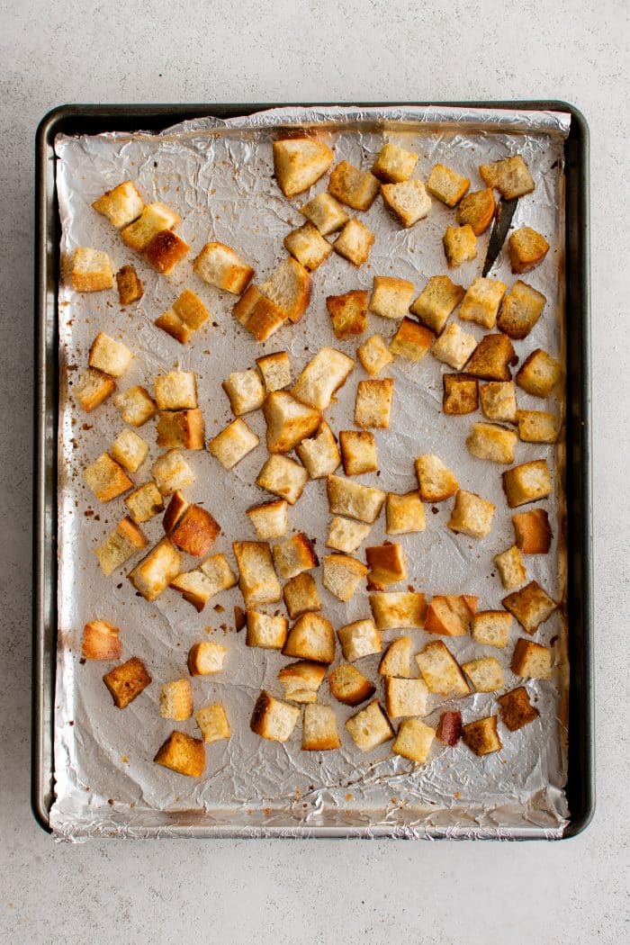 Homemade croutons on a large baking sheet lined with aluminum foil.